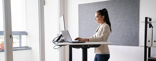 Uma mulher em pé diante de uma mesa usando um laptop.