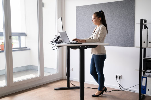 Uma mulher em pé diante de uma mesa usando um laptop.