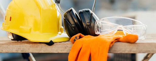 Um capacete amarelo, luvas e proteção auricular sobre uma mesa.