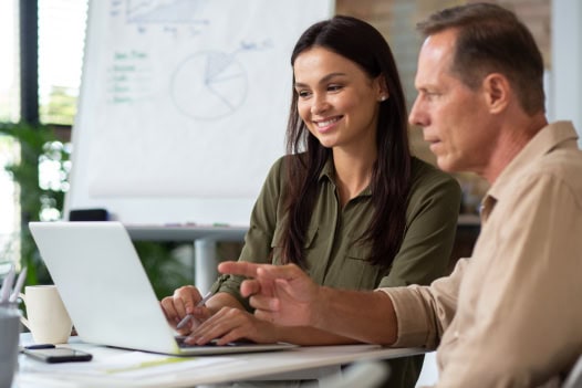 Um homem e uma mulher estão sentados à mesa com um laptop.