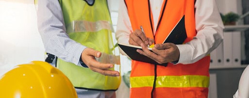 Dois trabalhadores da construção civil usando capacetes e coletes.