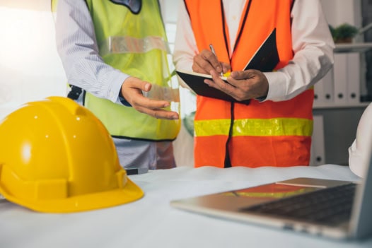 Dois trabalhadores da construção civil usando capacetes e coletes.